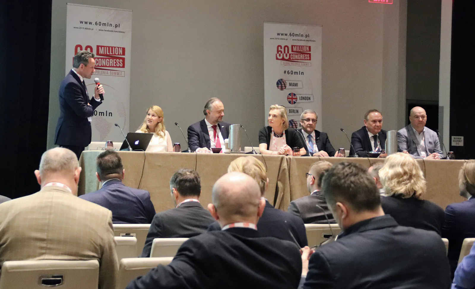Moderator with a microphone introducing seven panelists seated at a long table during the 60 Million Congress in Miami, 2019