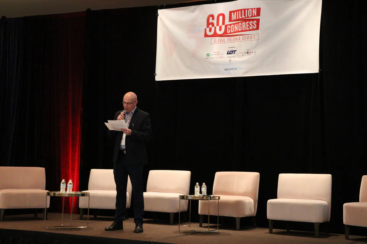 Speaker reading from notes into a microphone on the 60 Million Congress stage in front of empty panel chairs