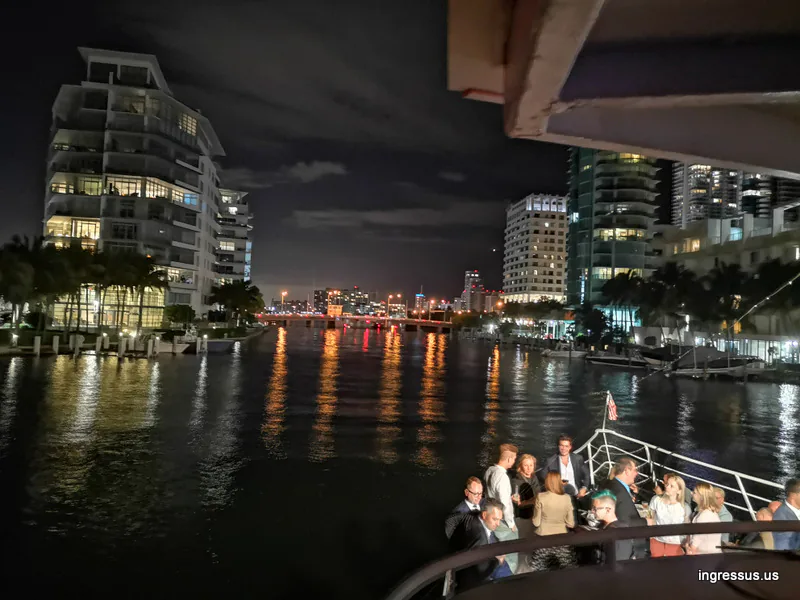 Congress guests on the bow of a boat cruising a Miami Beach waterway at night past lit high-rise buildings