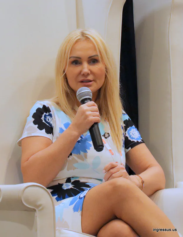 Panelist in a floral dress speaking into a microphone from a white armchair at the 60 Million Congress