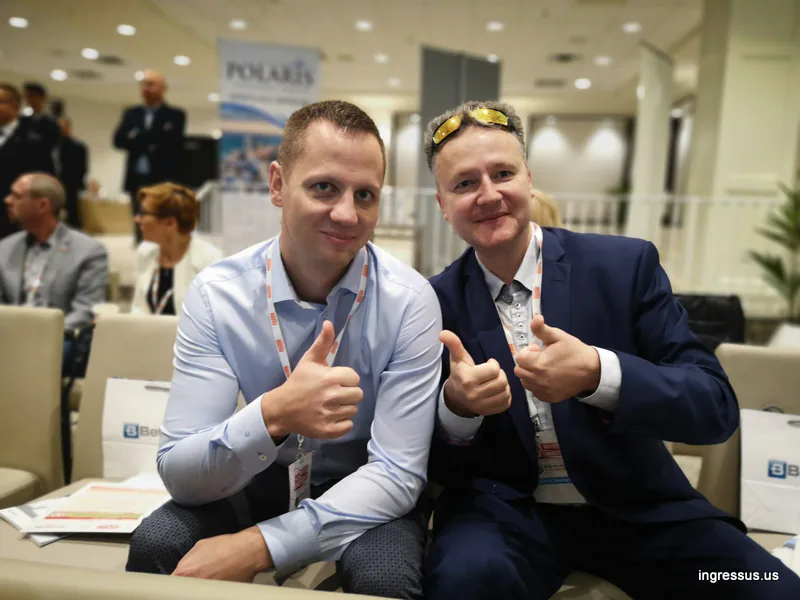 Two congress participants with badges giving a thumbs up from their seats in the conference hall