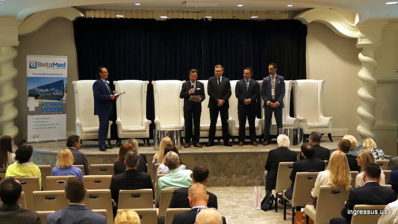Speakers standing on a stage with tall white armchairs during a session of the 60 Million Congress at the Eden Rock Hotel in Miami Beach