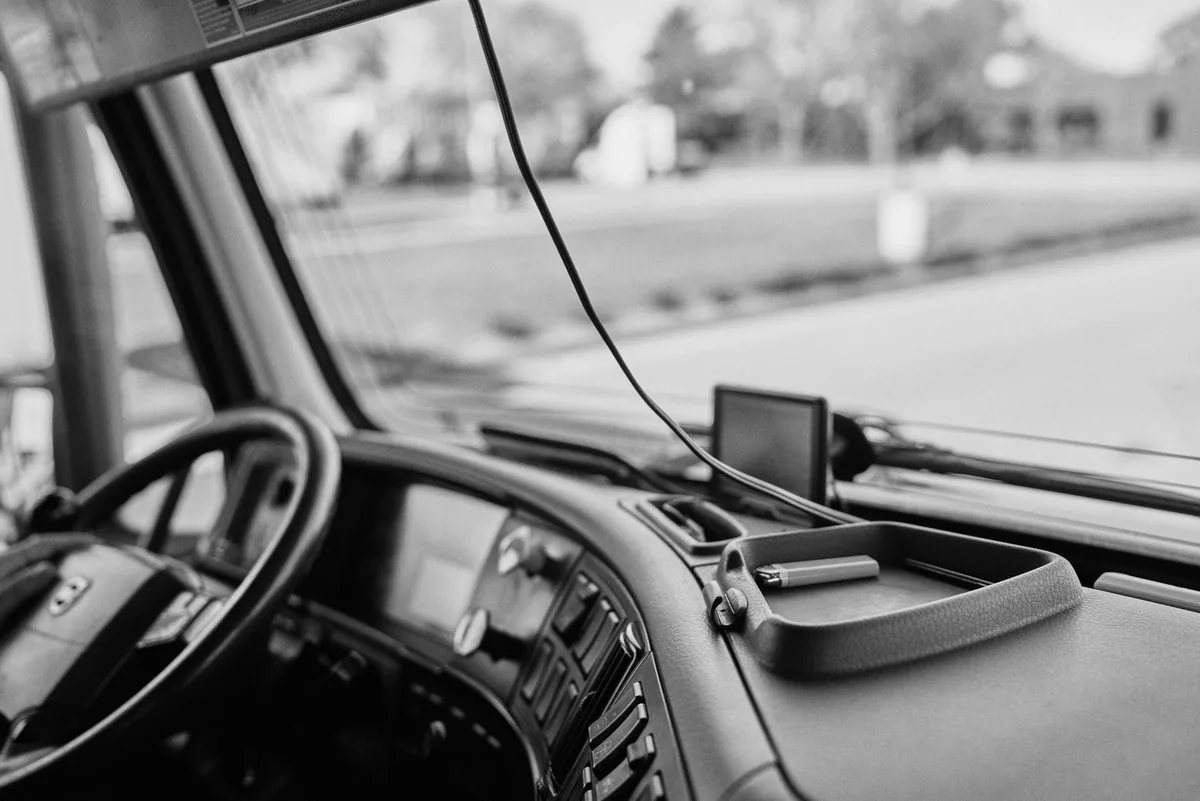 Black and white view from a truck cab across the dashboard and windshield, with a GPS unit on the dash