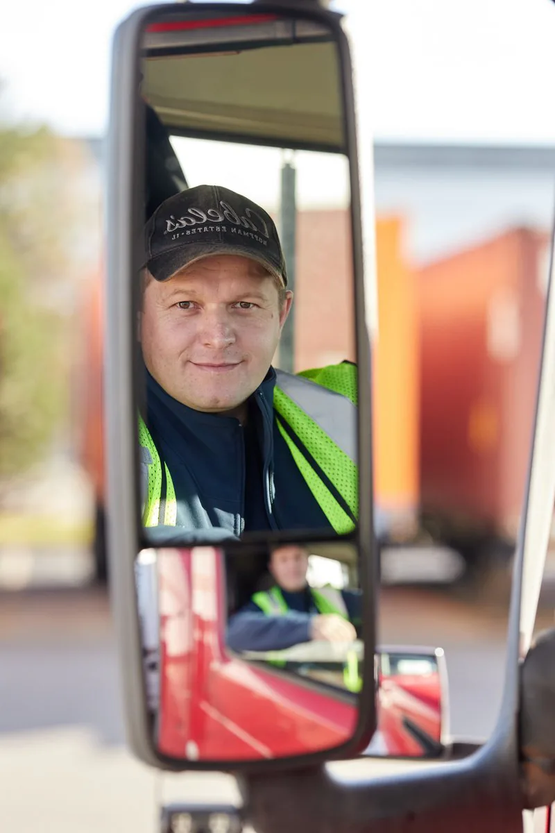 Driver in a cap and high-visibility vest reflected in the side mirrors of a red truck cab