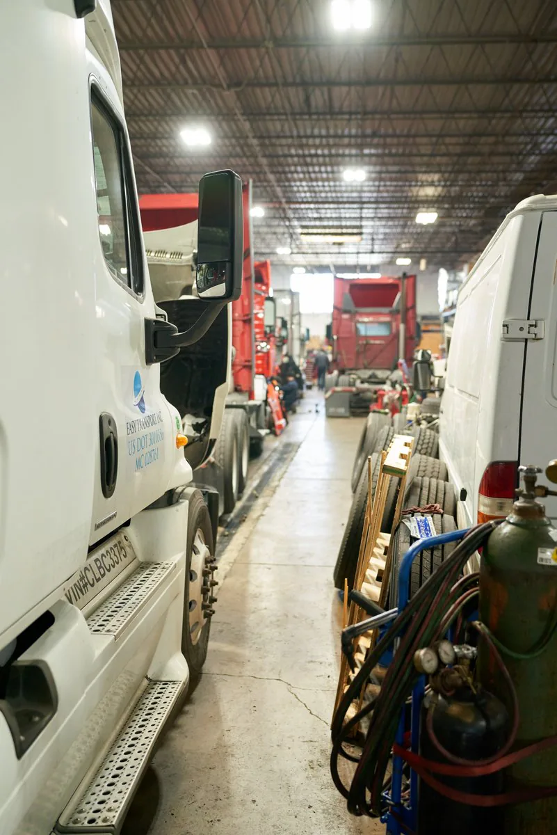 Truck repair shop with white and red semi-trucks, stacked tires and welding gas cylinders along the aisle