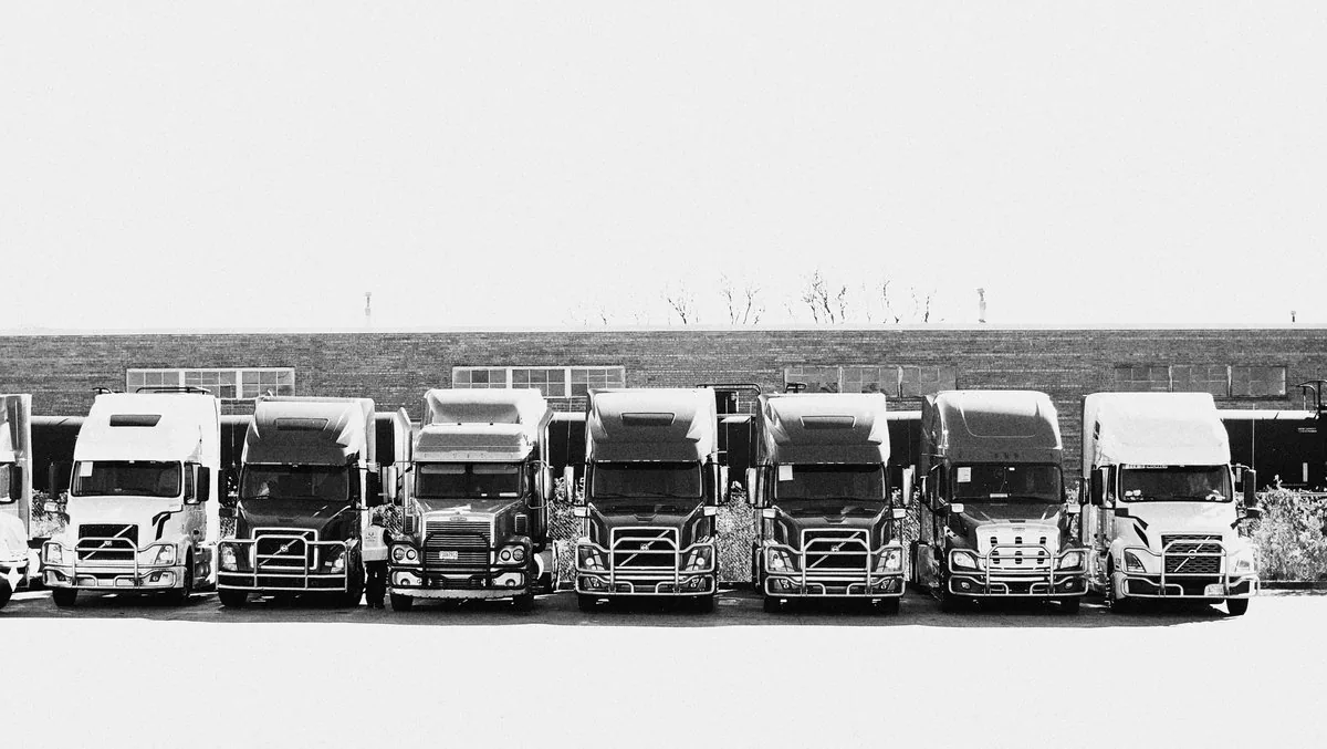 Black and white panorama of a row of semi-trucks parked side by side in front of a brick building