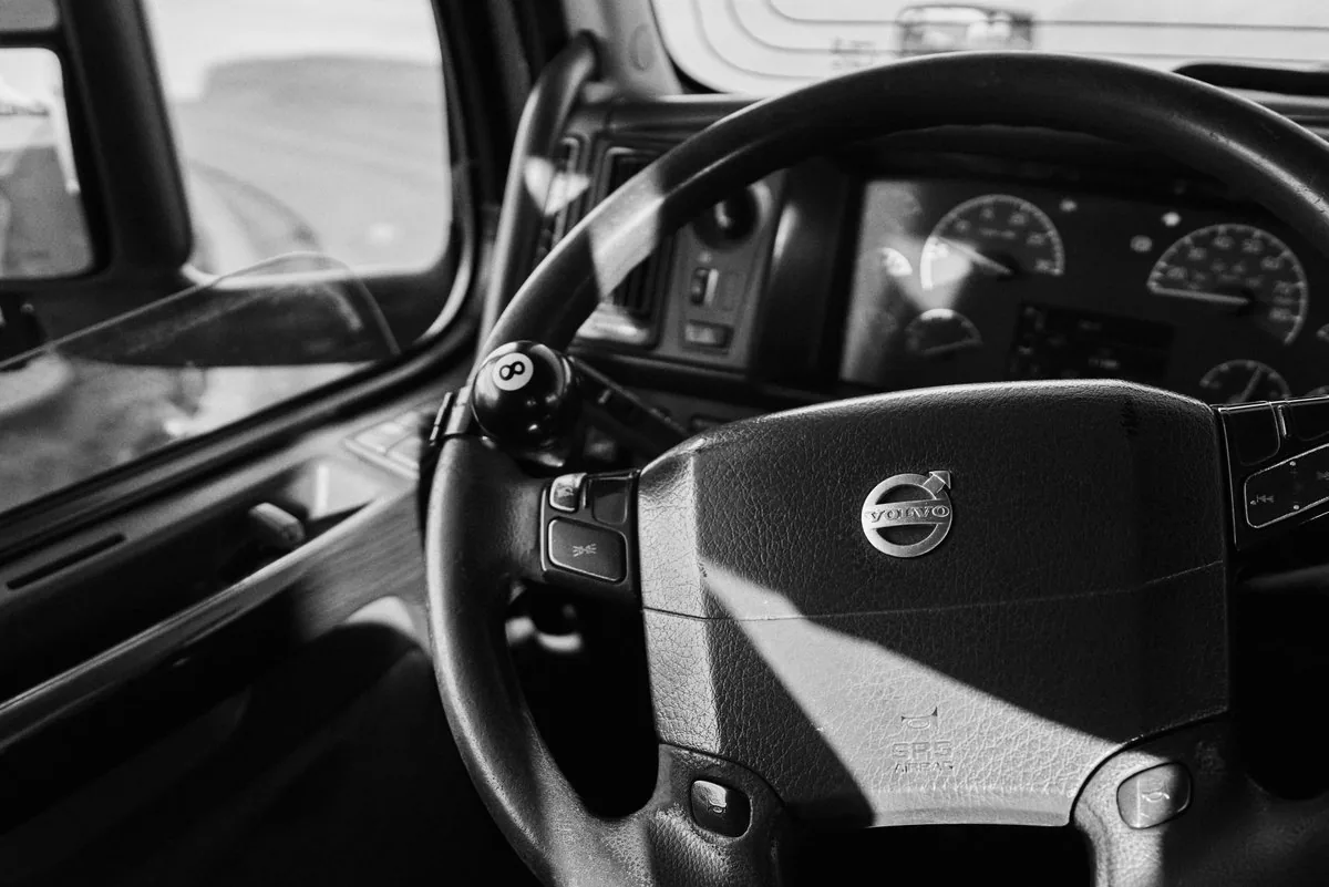 Black and white close-up of a Volvo truck steering wheel with an eight ball spinner knob and the dashboard gauges