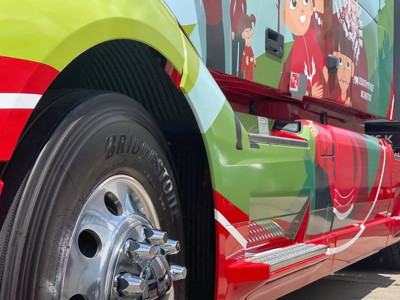 Close-up of the Arrow Trans Corp truck wrap by the front wheel, with illustrated family figures on the cab side