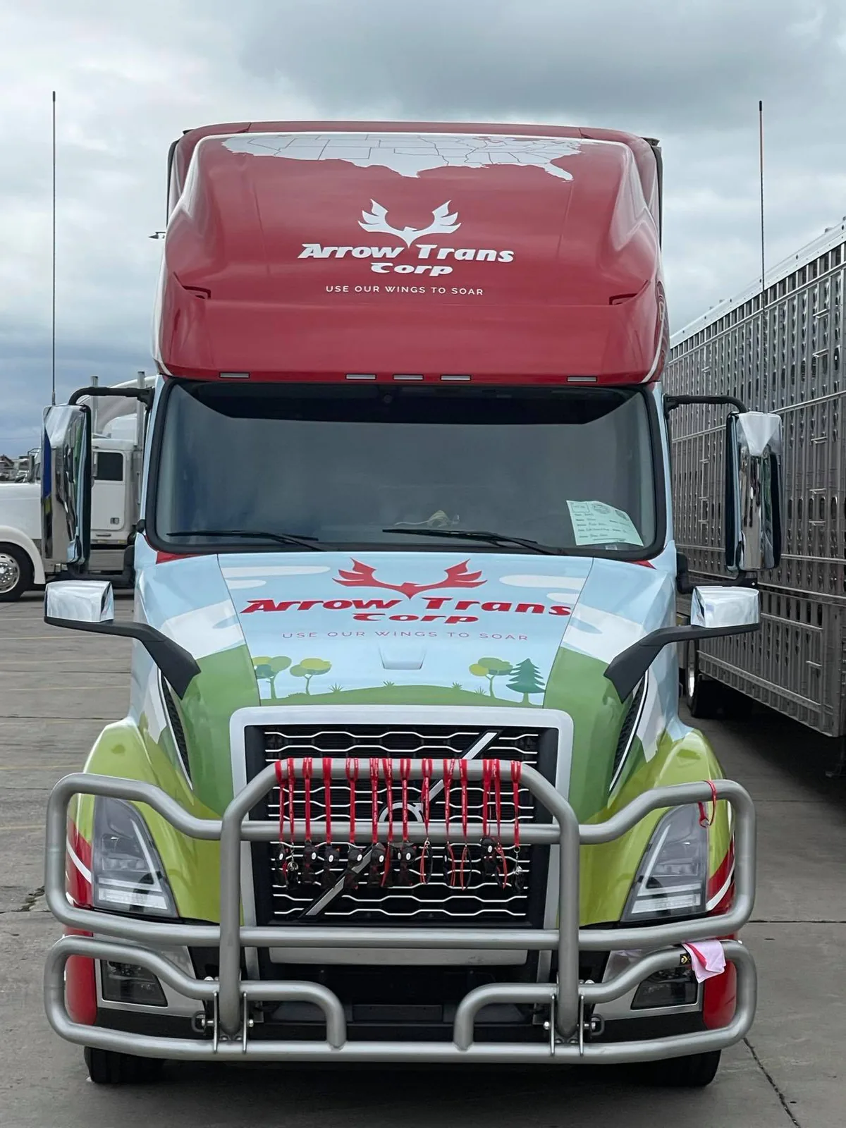 Front view of the wrapped Arrow Trans Corp truck with the red roof logo and a green illustrated hood in a truck yard