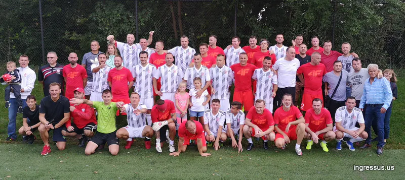 Large group photo of two amateur teams in red and striped kits on a soccer field during the Soccer Legends Cup promotion
