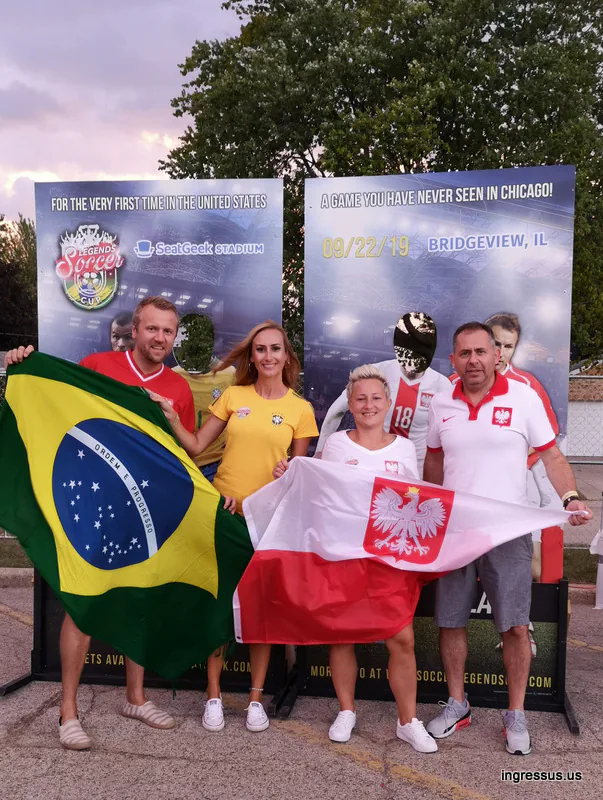 Four fans holding Brazil and Polish flags in front of the Soccer Legends Cup photo boards announcing the 09/22/19 match in Bridgeview