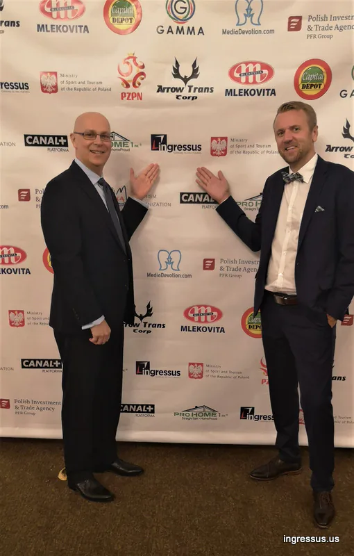 Two men pointing at the Soccer Legends Gala sponsor wall showing the Ingressus logo among partners such as PZPN, Canal+ and Mlekovita