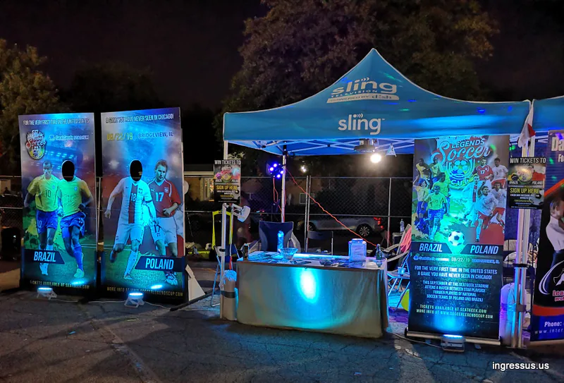 Soccer Legends Cup promo booth at night with a Sling TV tent, Brazil and Poland photo boards and a ticket giveaway sign-up
