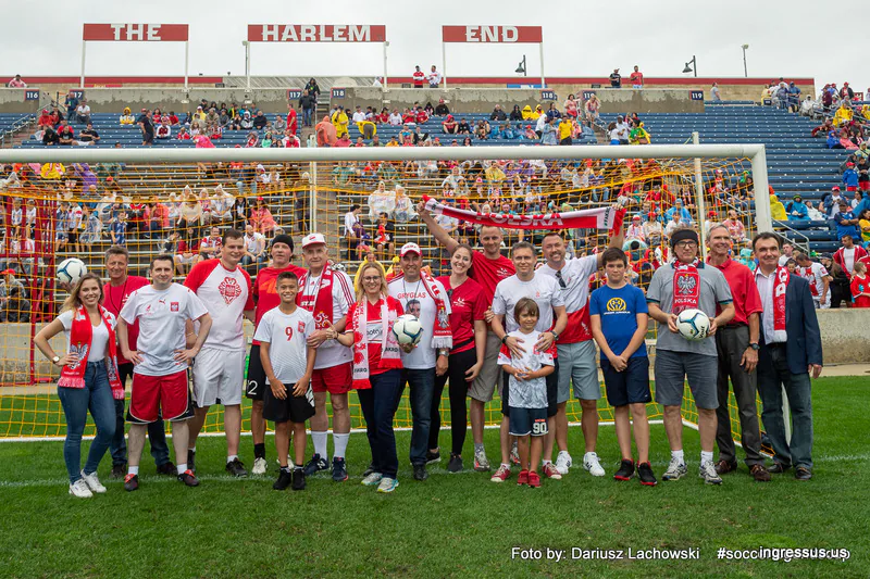Fans in Polish scarves and jerseys posing with soccer balls in front of the goal and The Harlem End stand at SeatGeek Stadium