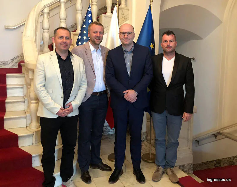 Four men posing by a marble staircase with U.S., Polish and European Union flags during the Soccer Legends Cup preparations