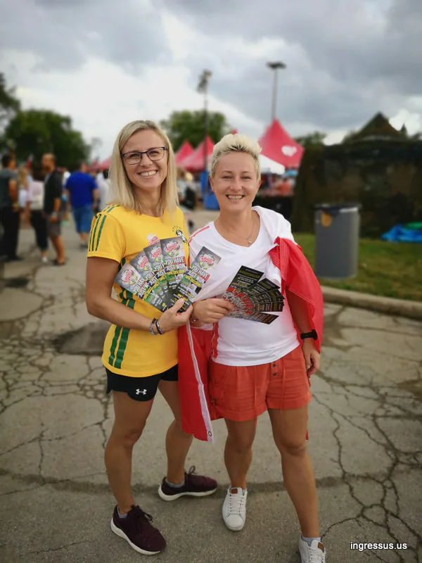 Two women in Brazil and Poland shirts holding fanned-out Soccer Legends Cup flyers at an outdoor festival