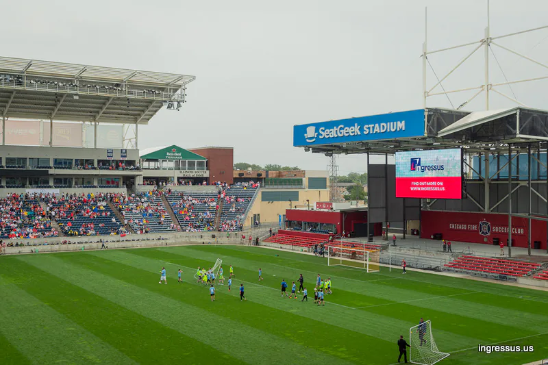 Youth soccer game on the pitch at SeatGeek Stadium before the Legends match, with an Ingressus ad on the video board