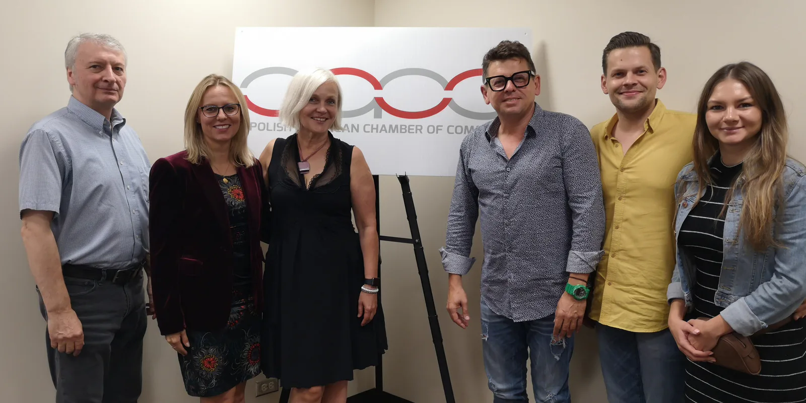 Six people at a meeting with the Polish American Chamber of Commerce, posing by the PACC logo sign in Chicago, August 2019