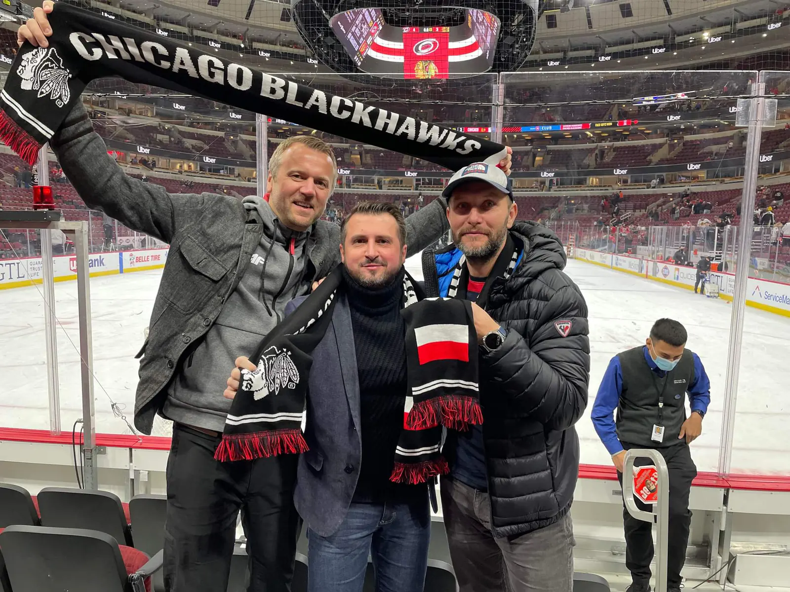 Three men holding up Chicago Blackhawks scarves with the Polish flag by the rink at the United Center on Polish Heritage Night