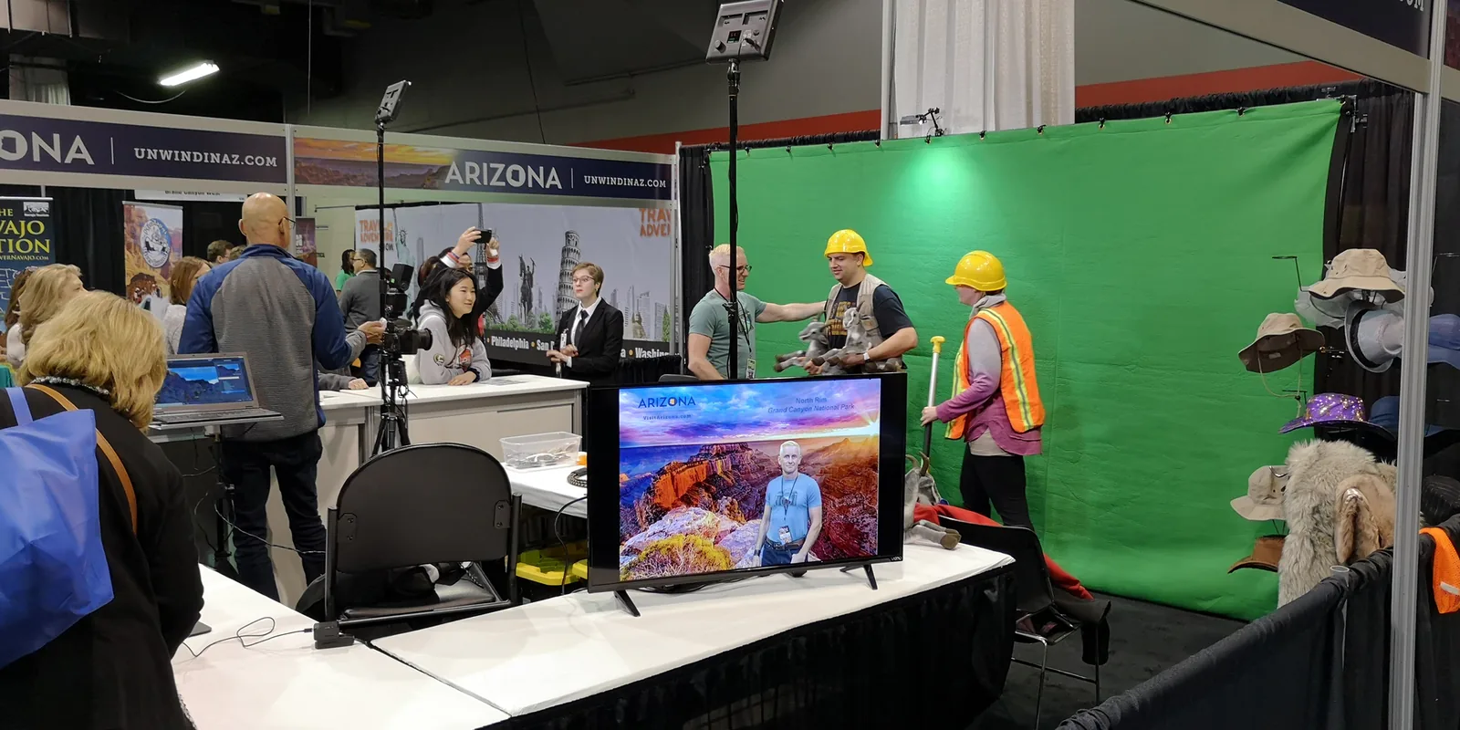 Visitors in hard hats posing at the Arizona booth green screen photo station, with a Grand Canyon composite on a screen