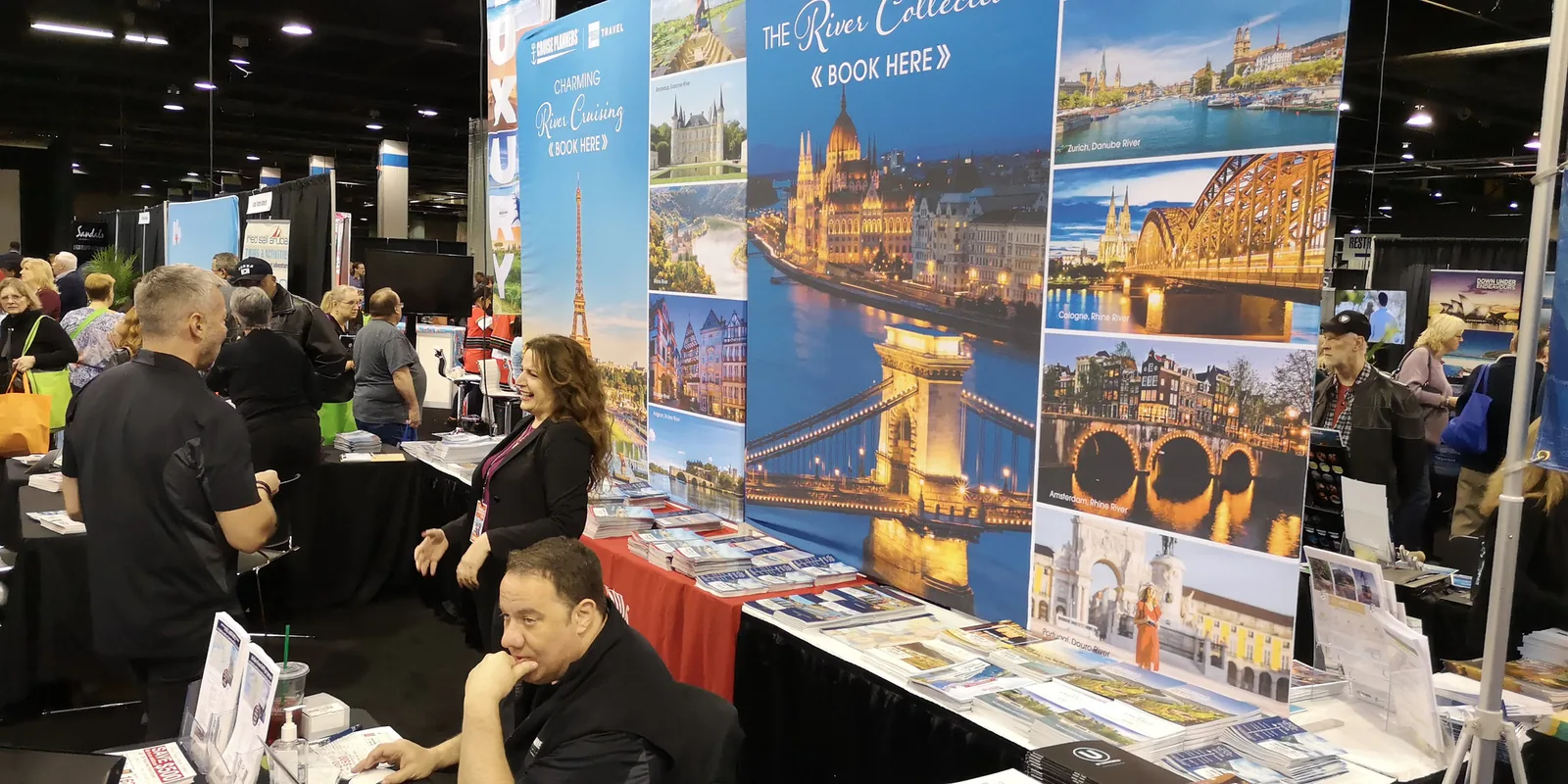 Exhibitors and visitors at a river cruise booth with European city posters and brochures at the Chicago Travel & Adventure Show 2019
