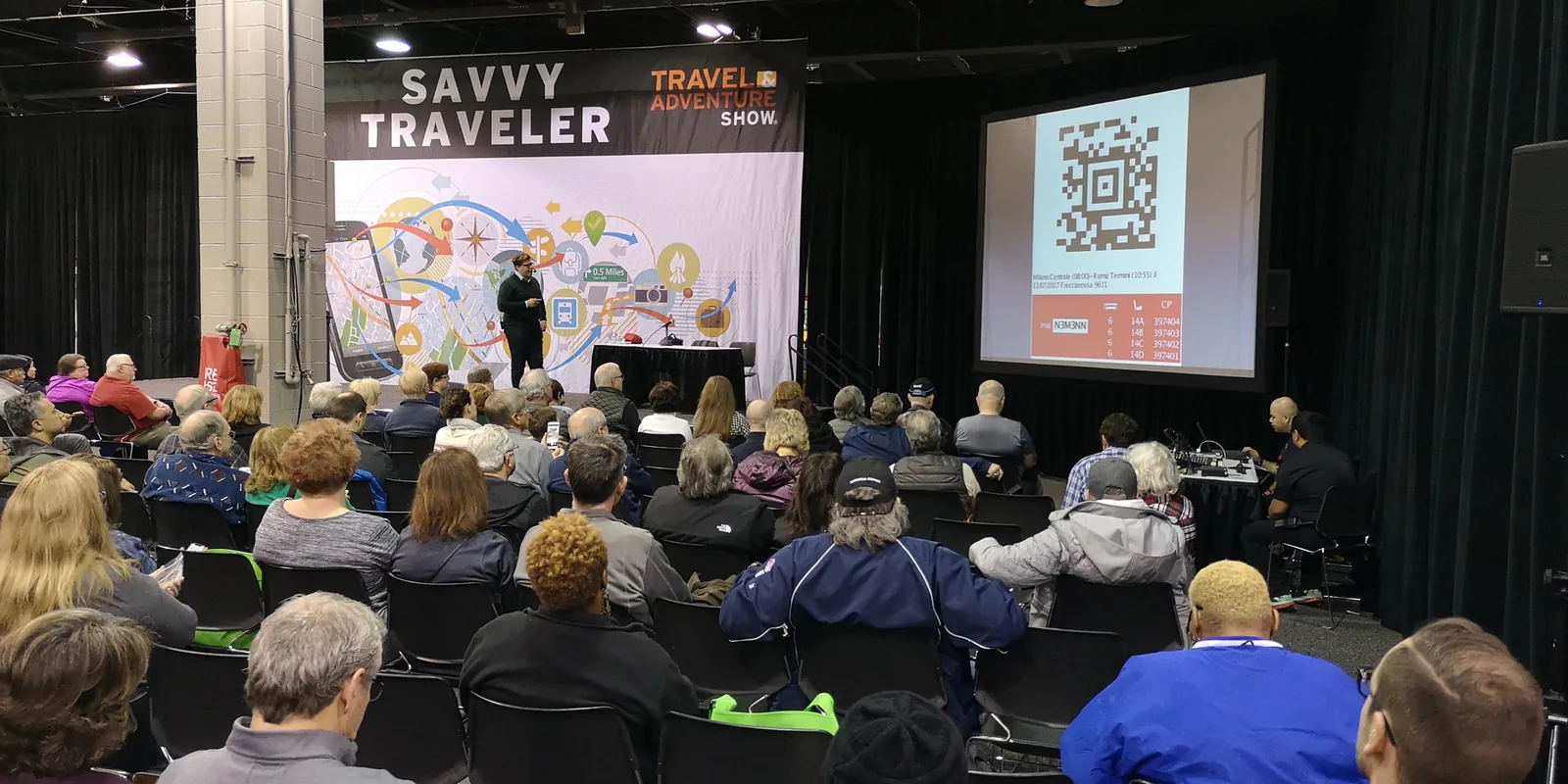 Speaker presenting on the Savvy Traveler Theater stage to a seated audience at the Chicago Travel & Adventure Show 2019