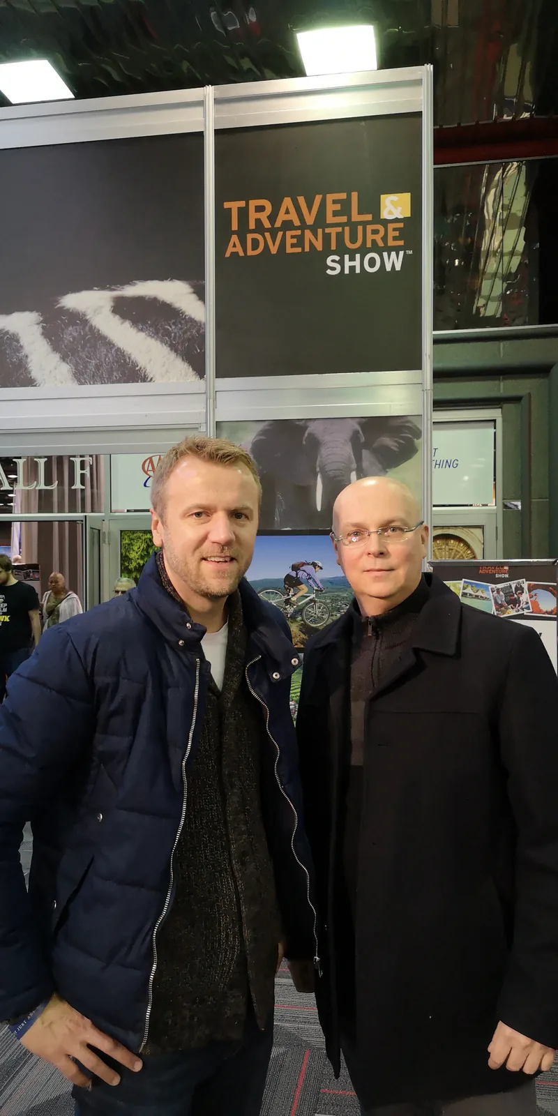 Two men posing under the Travel & Adventure Show sign at the Donald E. Stephens Convention Center in Rosemont, January 2019