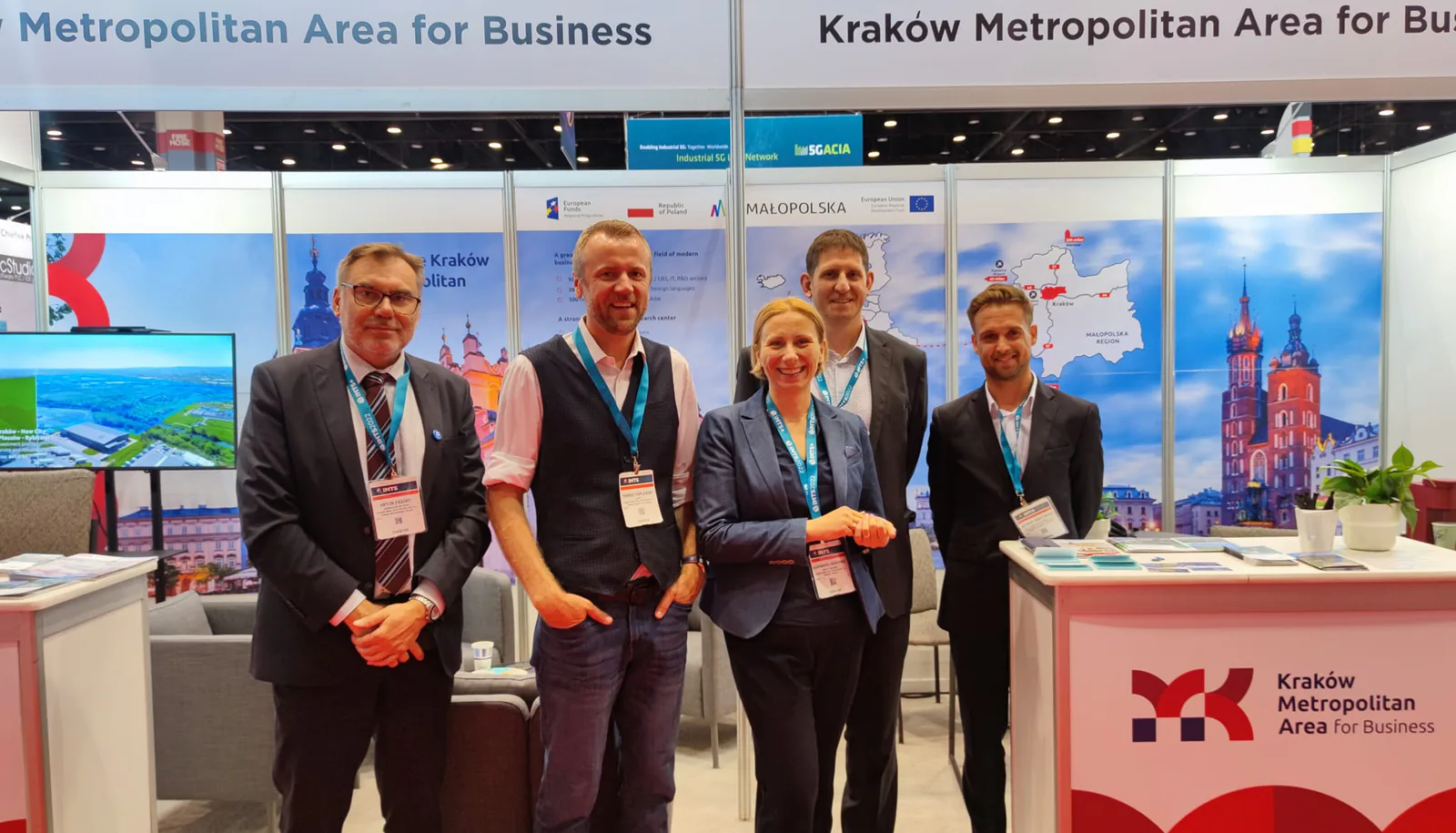 Five exhibitors at the Kraków Metropolitan Area for Business booth at IMTS 2022, with Małopolska maps and Kraków images behind