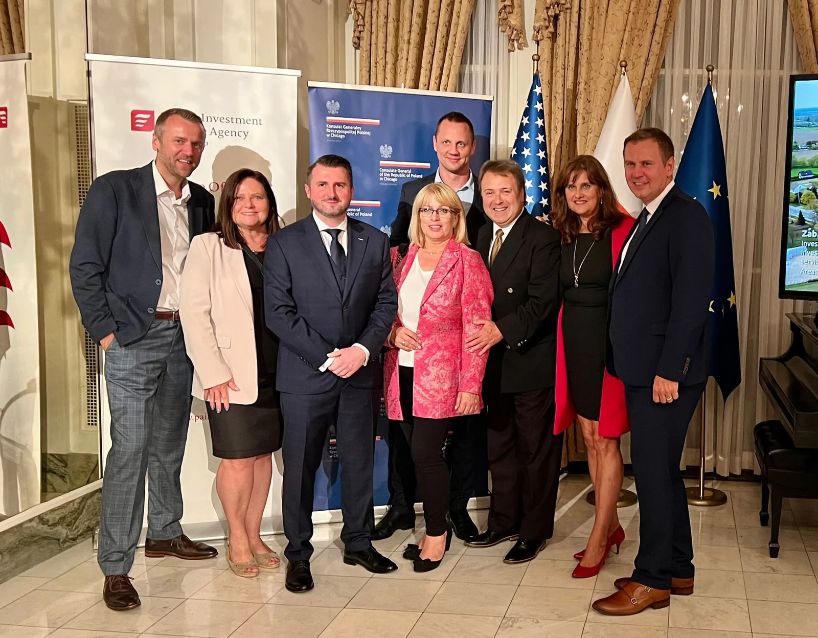 Group posing in front of Consulate General of the Republic of Poland in Chicago and Polish Investment and Trade Agency banners