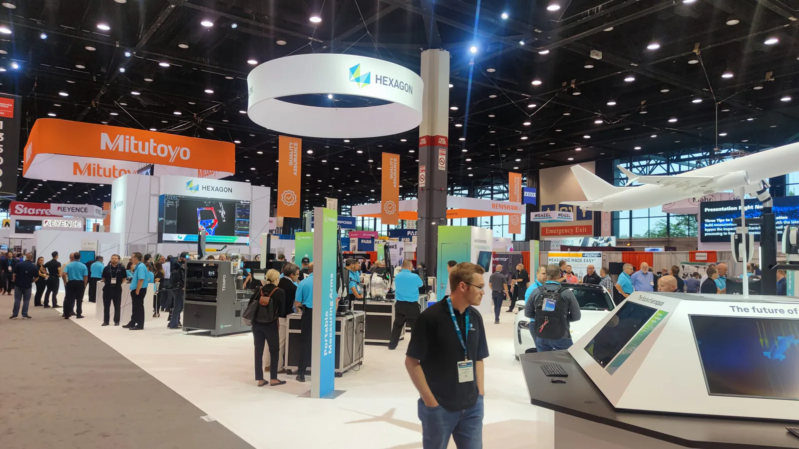 Busy IMTS 2022 exhibition hall in Chicago with Hexagon and Mitutoyo stands and a model aircraft on display