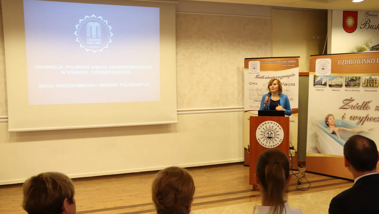 Anna Krupka speaking at the Busko-Zdrój seminar beside a slide on promoting Polish health services in the United States