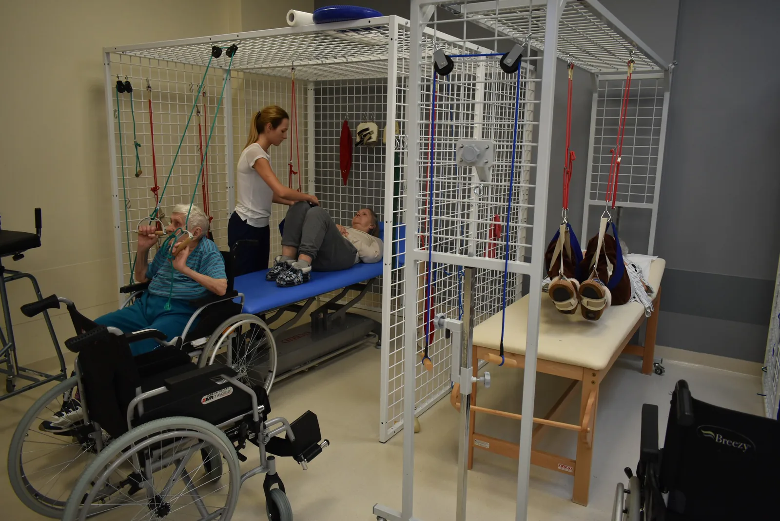 Physiotherapist working with a patient in the TriVita rehabilitation gym, with suspension therapy frames and wheelchairs