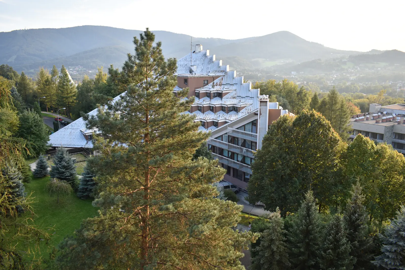 Pyramid-shaped sanatorium of Uzdrowisko Ustroń among pine trees, with the Beskid mountains in the background