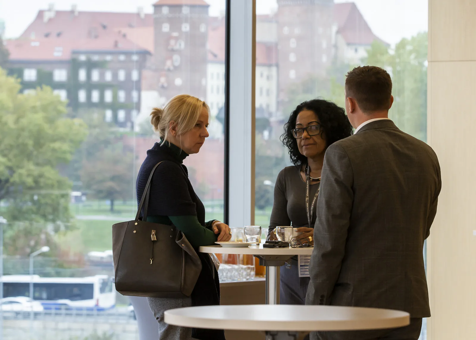 Three participants talking at a high table by a large window during a congress coffee break at ICE Kraków