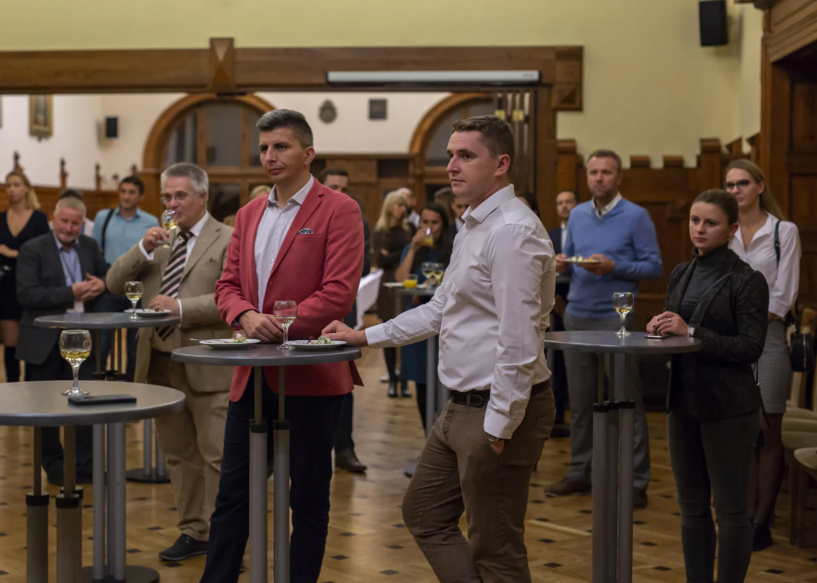 Guests with glasses of wine at high tables listening to a speech at the congress evening reception in a wood-paneled hall
