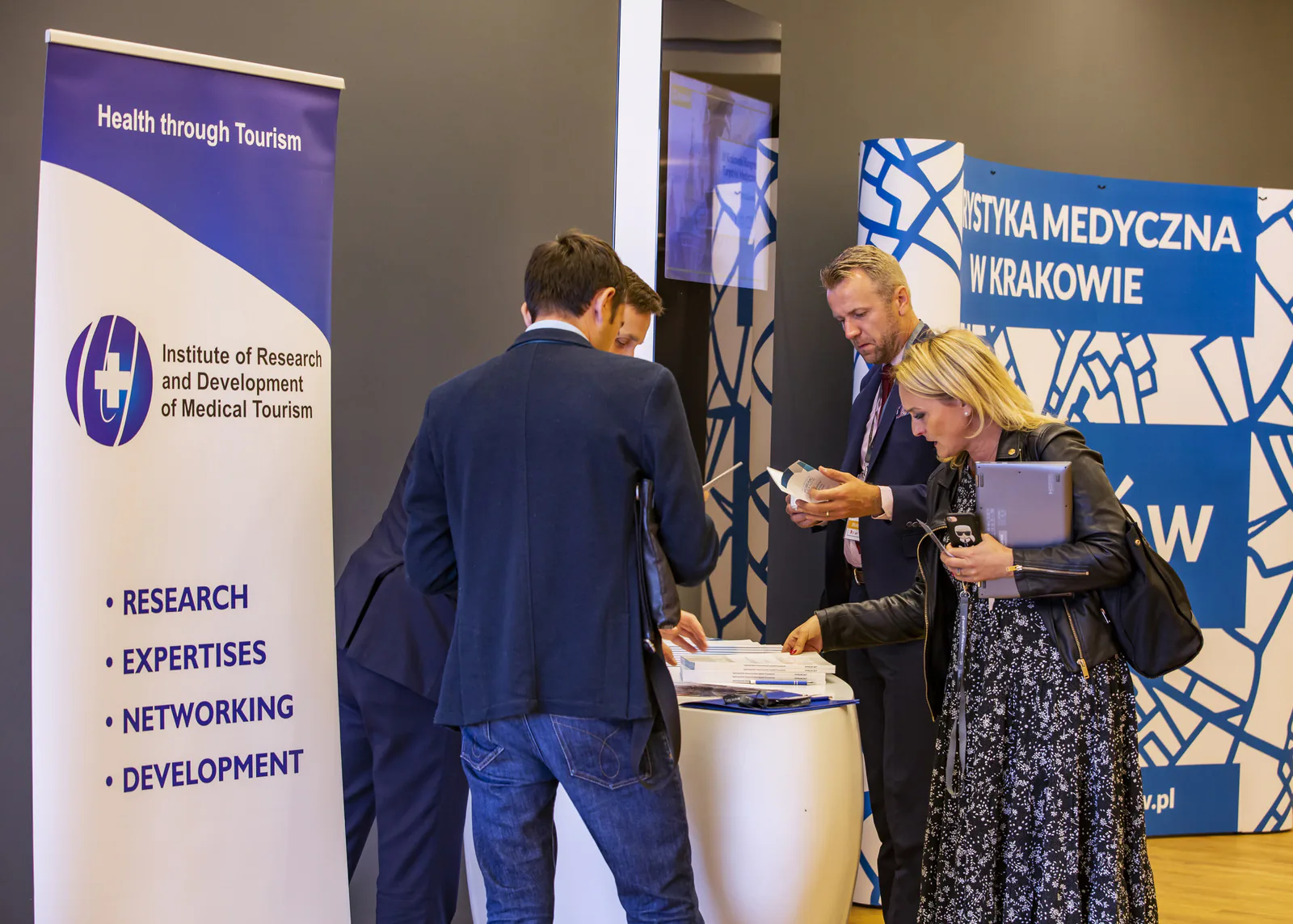 Participants picking up brochures at the Institute of Research and Development of Medical Tourism stand next to a Medical Tourism in Kraków wall