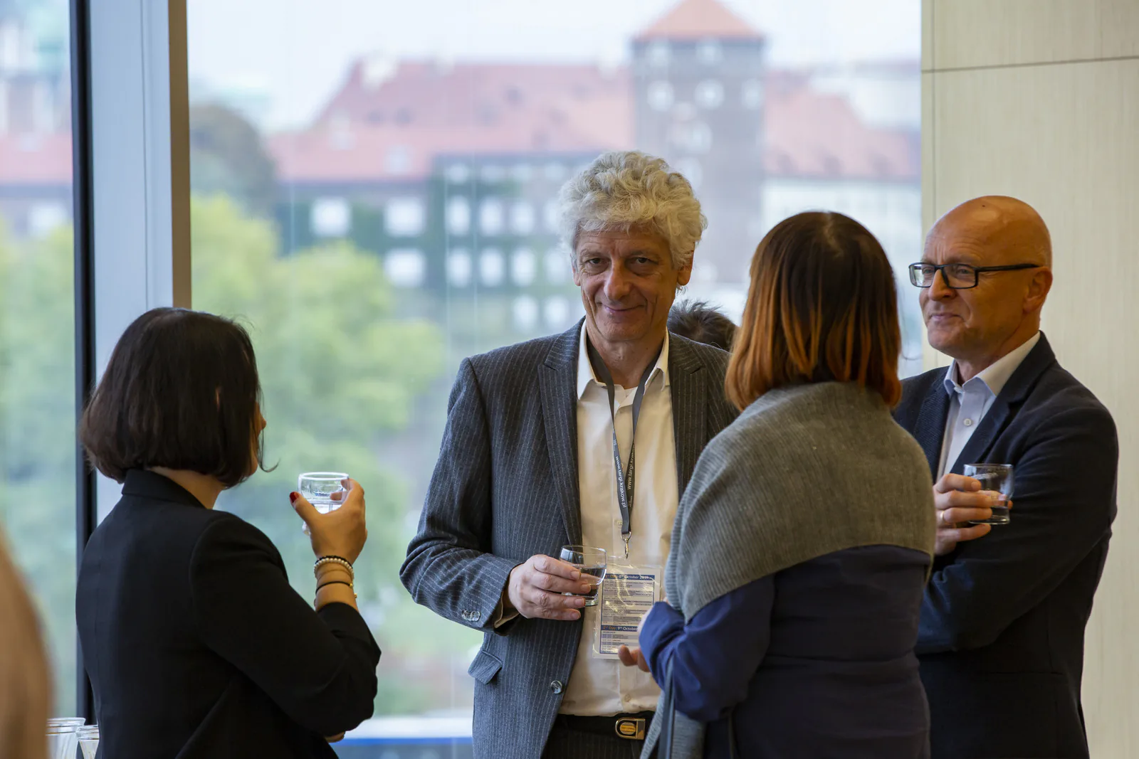 Congress guests chatting with glasses of water by a window overlooking Kraków during a networking break