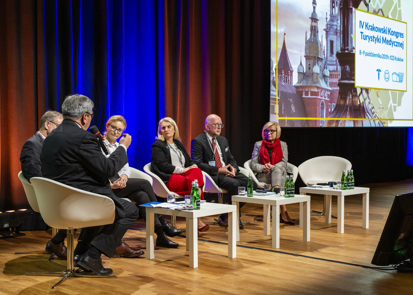 Panel discussion on stage below a screen showing the title of the 4th Kraków Medical Tourism Congress