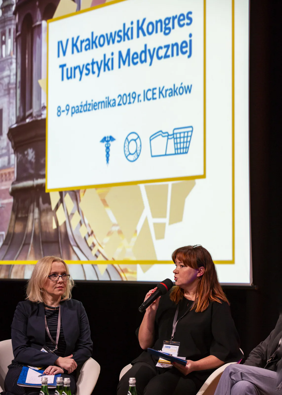 Panelist speaking into a microphone in front of the 4th Kraków Medical Tourism Congress title screen