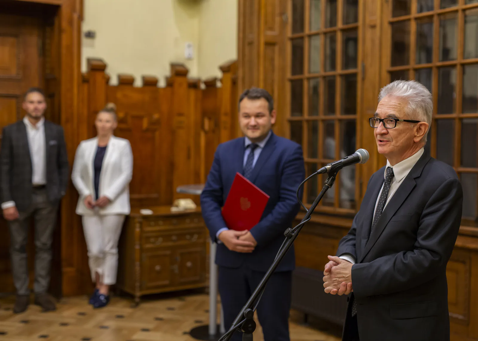 Host giving a welcome speech at a microphone during the congress reception in a historic wood-paneled hall