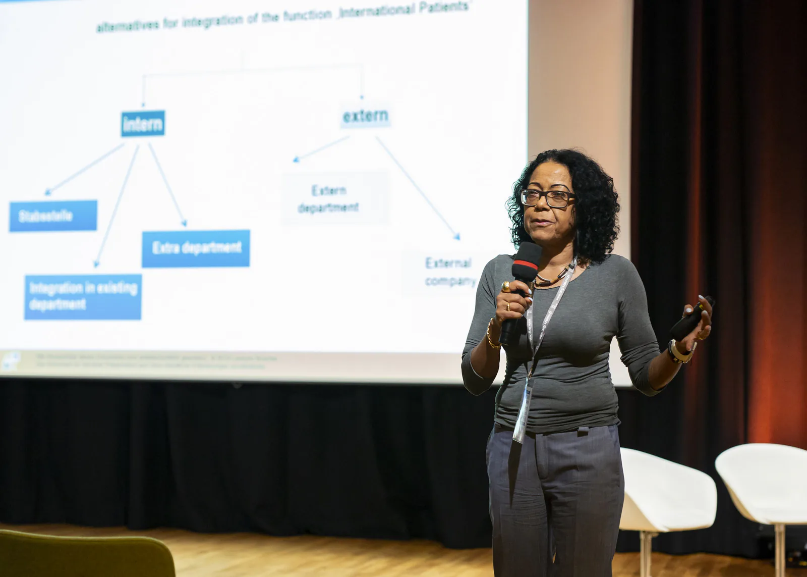 Speaker with a microphone presenting a slide on ways to set up an international patients department