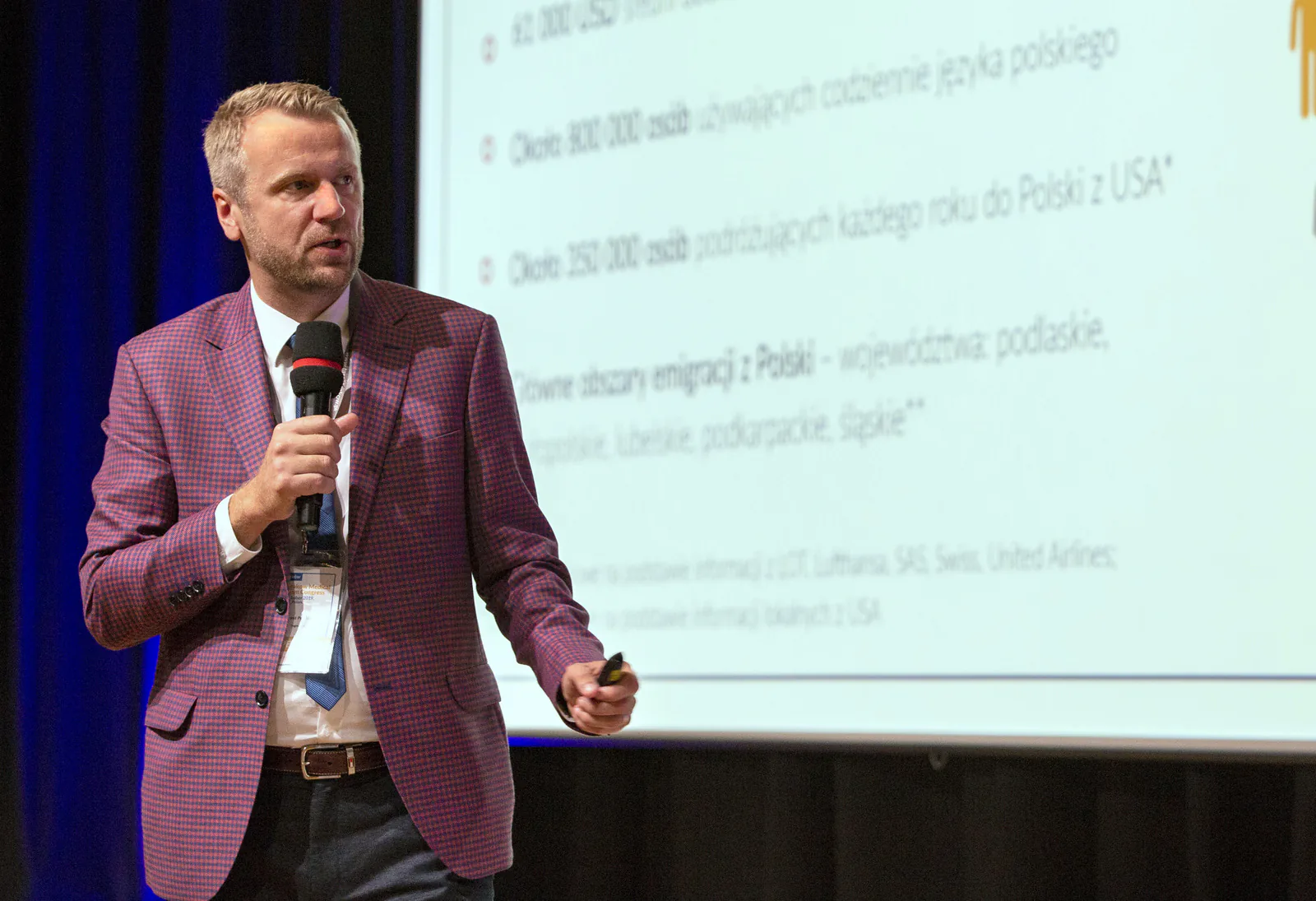 Speaker with a microphone presenting a slide with figures on Polish speakers in the USA and yearly travel to Poland