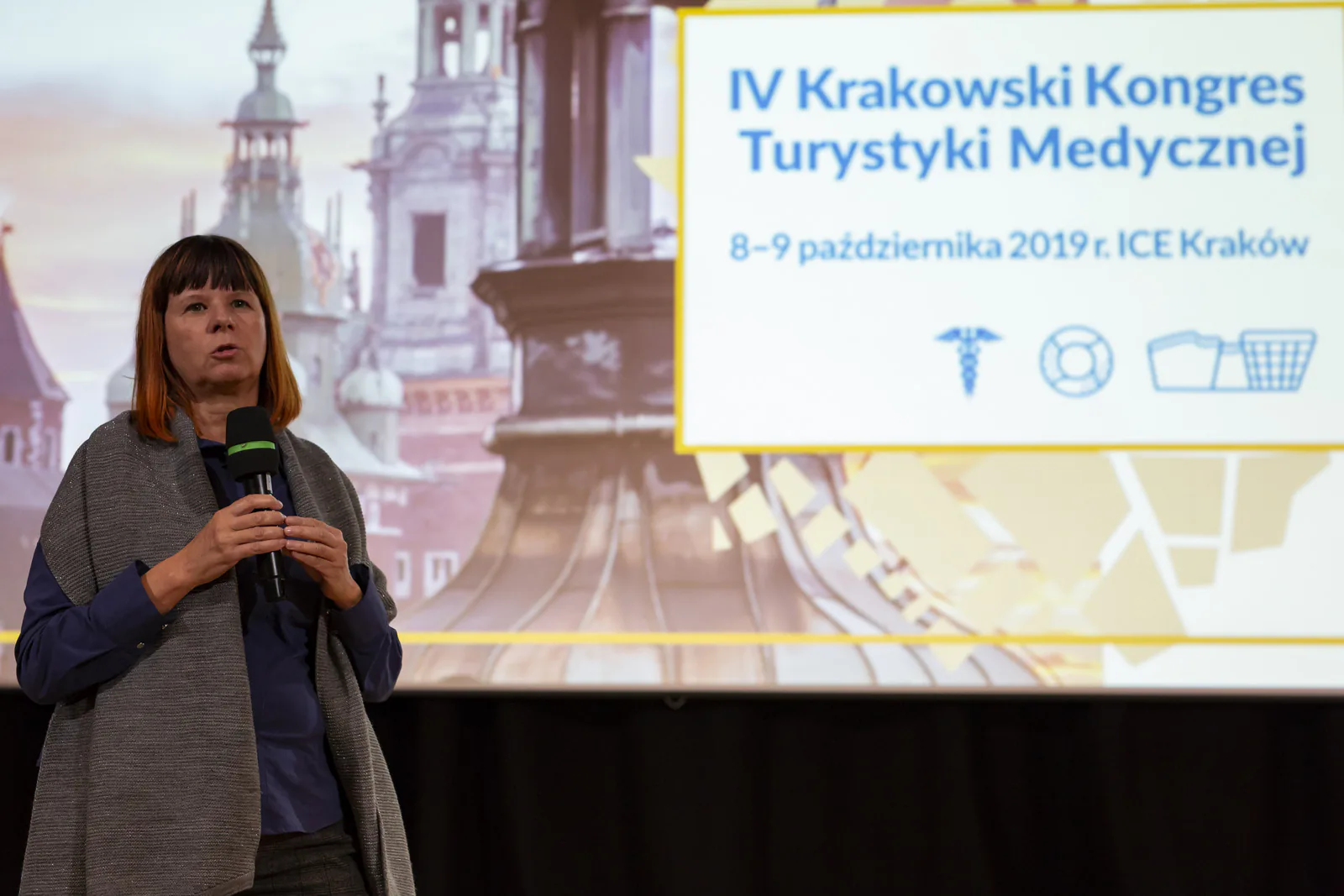 Participant speaking into a microphone in front of the 4th Kraków Medical Tourism Congress title screen