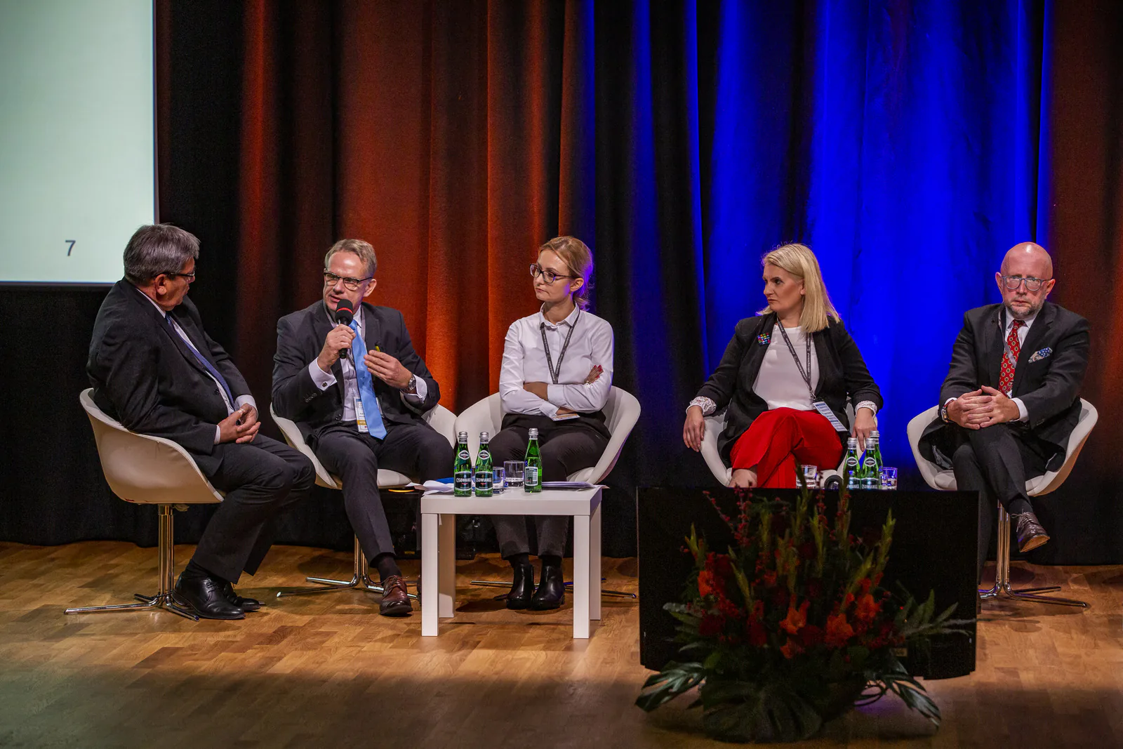 Five panelists in white chairs on a stage with red and blue curtains during a discussion at the Kraków medical tourism congress