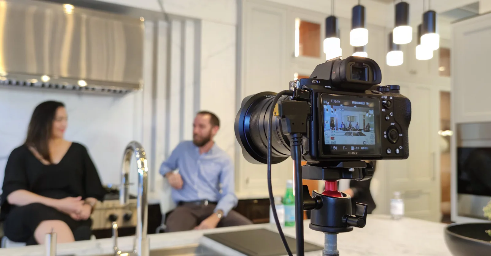 Sony camera on a stand filming two guests talking at a kitchen island during a live stream production