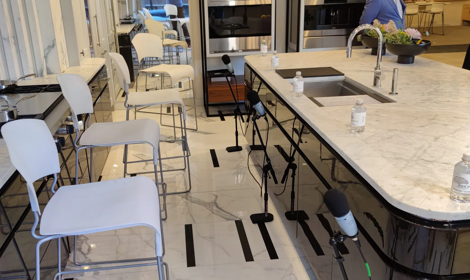 Microphones on stands set up around a marble kitchen island in a showroom, ready for a live streamed event