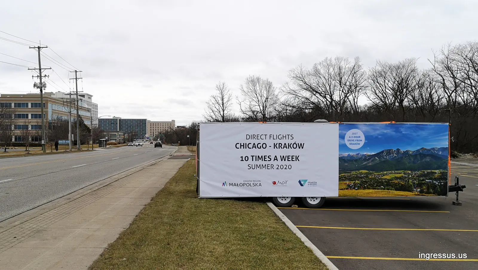 Outdoor banner trailer for Chicago to Kraków direct flights parked by the main road leading to the Rosemont convention center