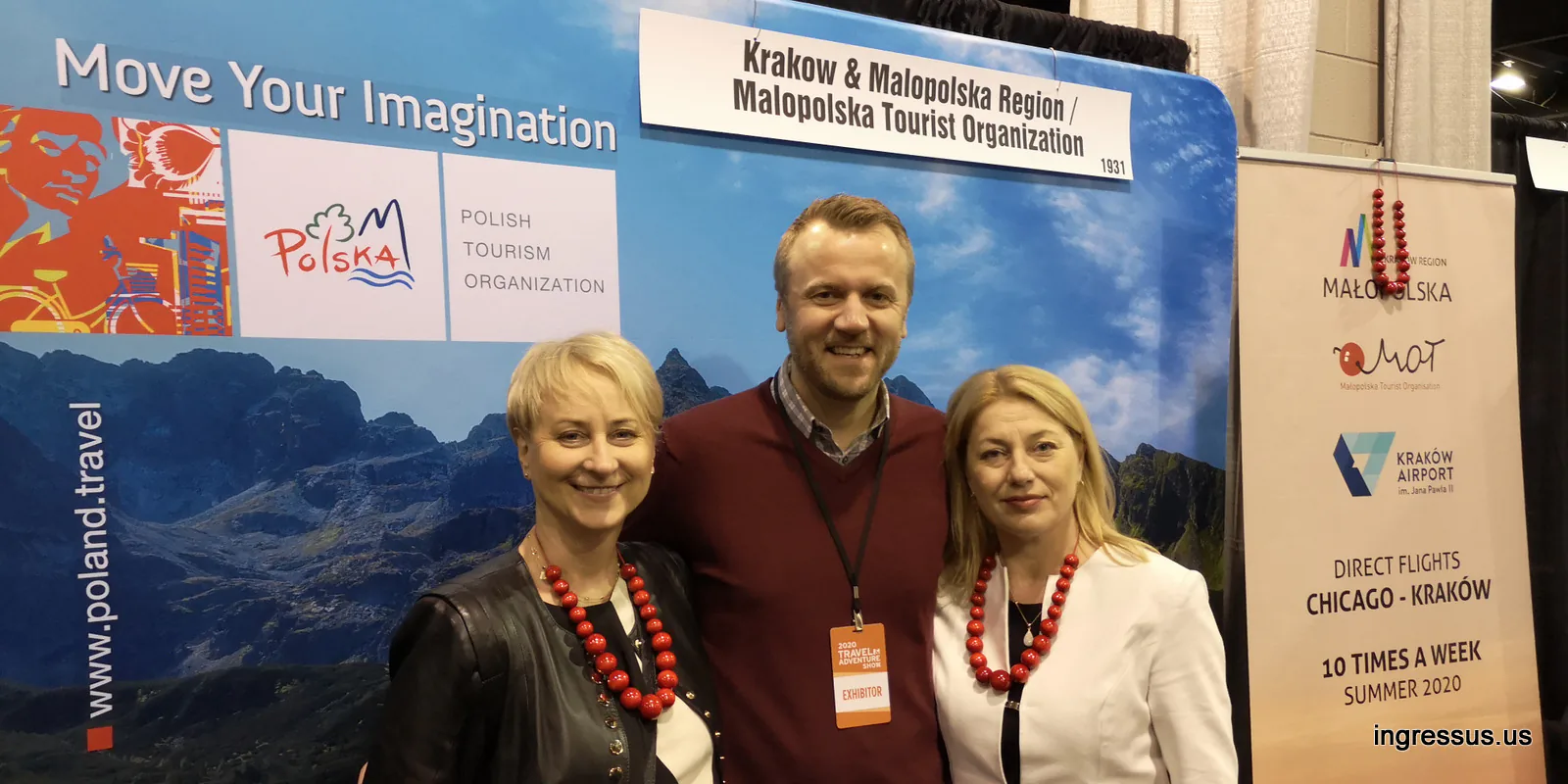 Two women in red coral necklaces and an exhibitor at the Kraków and Małopolska booth, next to a Chicago to Kraków direct flights banner