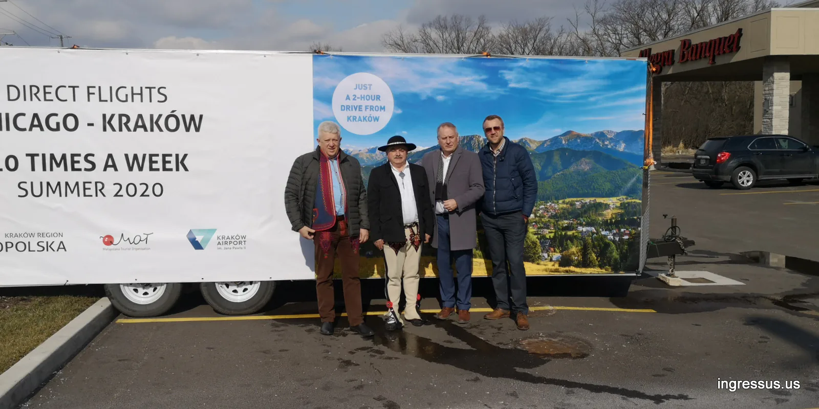 Four men, one in a Polish highlander outfit, by a banner trailer advertising direct flights Chicago to Kraków 10 times a week in summer 2020