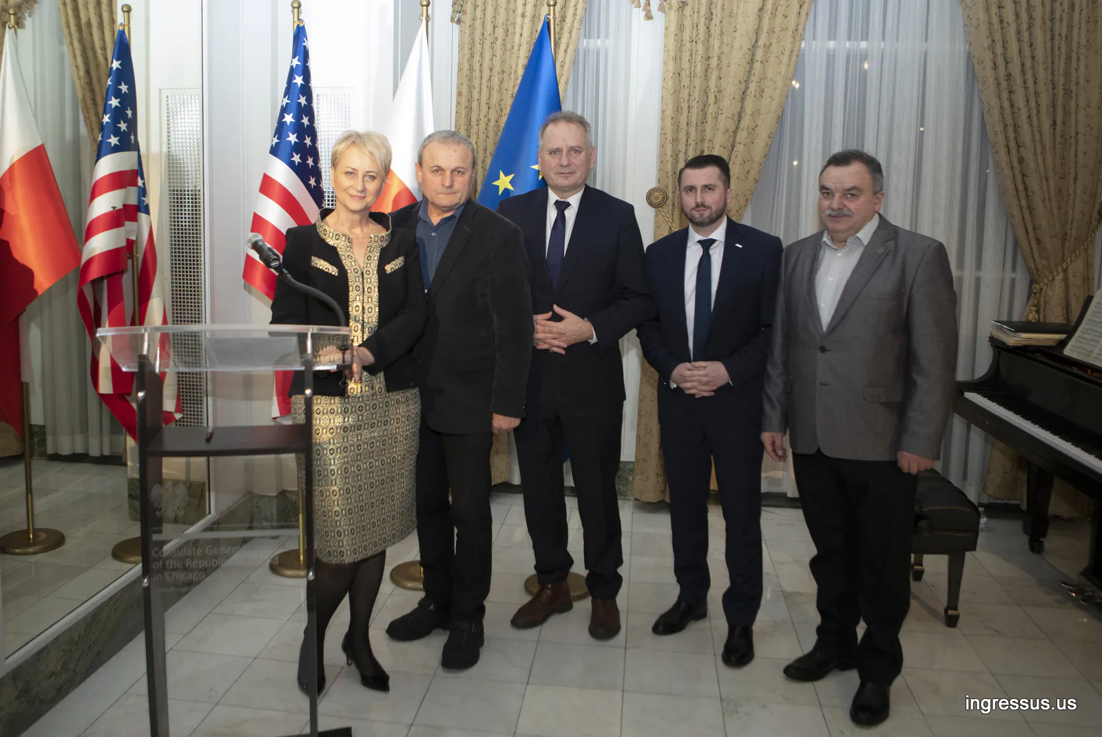 Five people posing by the podium and flags at the Polish Consulate General in Chicago, next to a grand piano